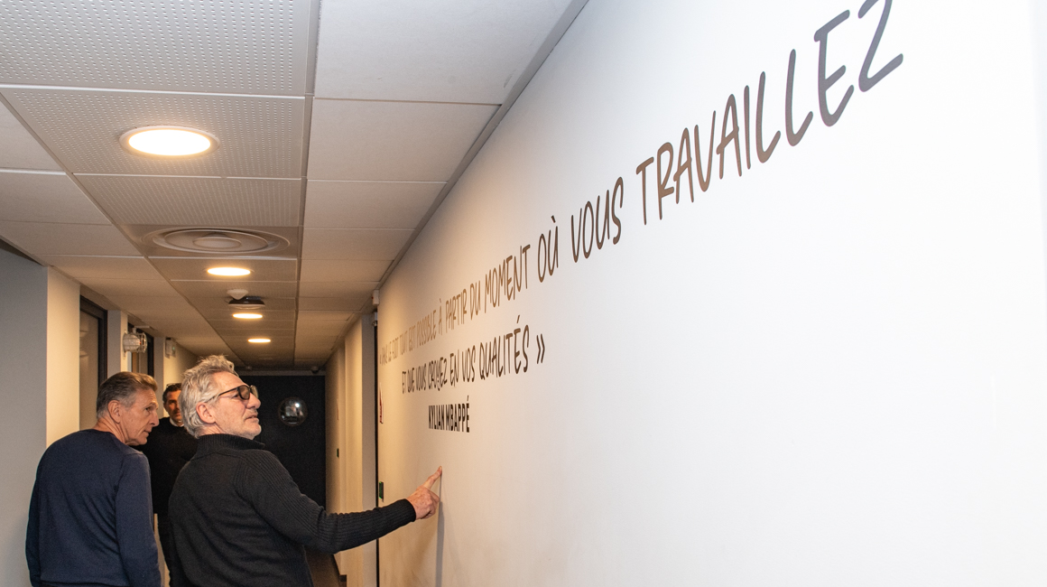 Jean-Luc Ettori et Claude Puel devant une citation de Kylian Mbappé sur un mur de La Diagonale.
